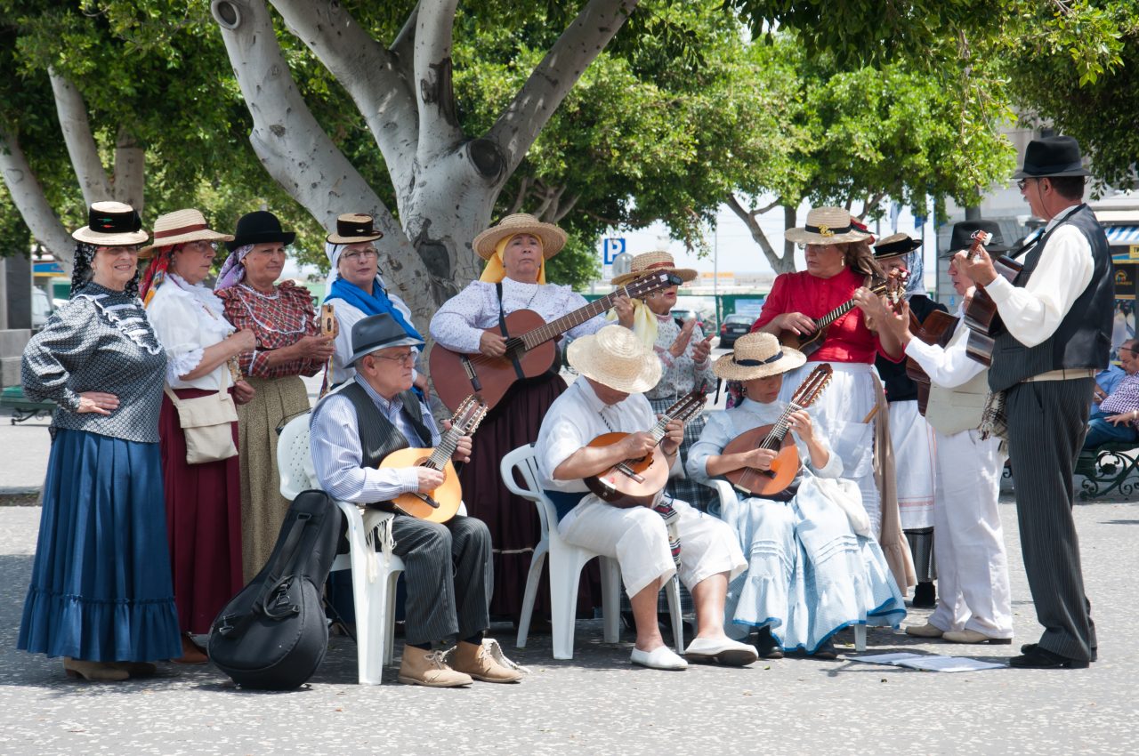 Canarian people wearing traditional outfits and playing music.